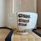 Angled view of the hand-painted matcha bowl showing the koinobori carp streamers, white cloud motifs, and multicolored band near the base.