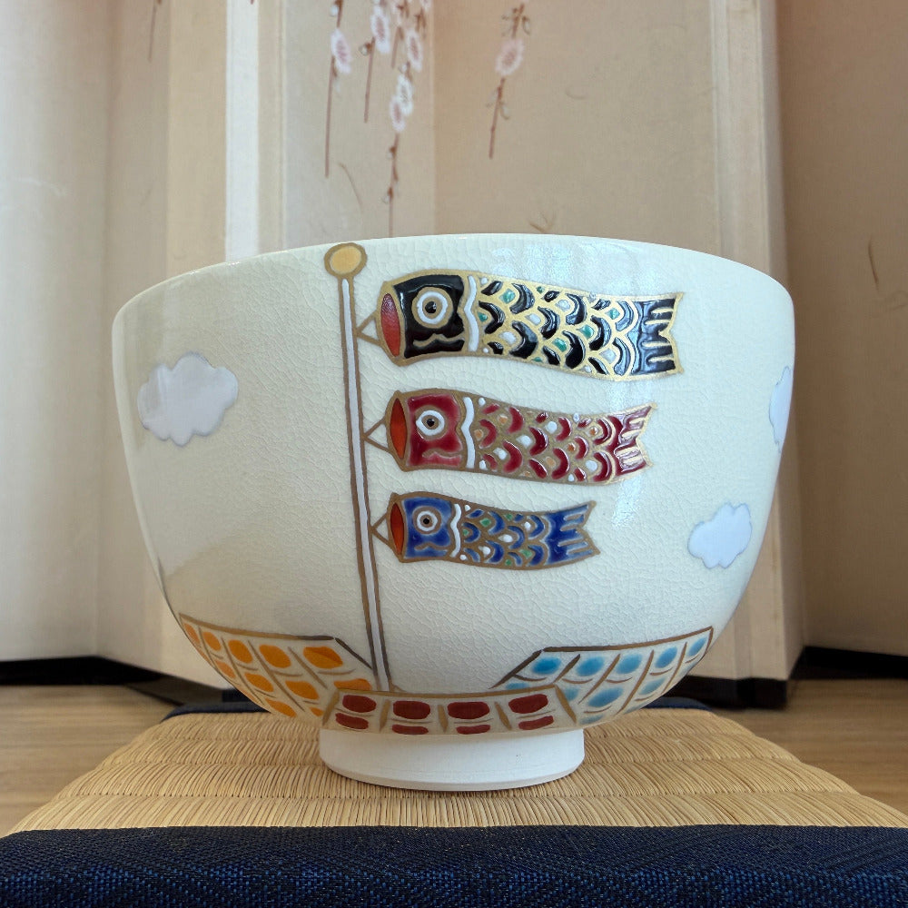 Front view of a hand-painted Kyo Ware matcha bowl decorated with black, red, and blue koinobori carp streamers, white clouds, and colorful geometric accents.