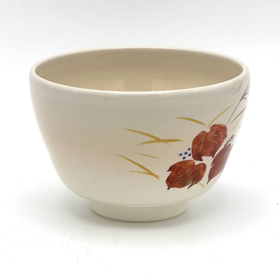 Side view of the hand-painted Kyo-yaki chawan showing red ivy leaves and slender autumn grasses against the warm ivory glaze