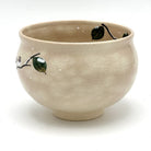 Angled view of the Kyo-yaki Eda ni Suzume chawan showing its rounded profile, warm beige glaze, and partial hand-painted branch and green leaf motif
