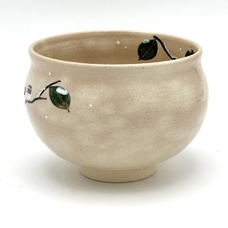Angled view of the Kyo-yaki Eda ni Suzume chawan showing its rounded profile, warm beige glaze, and partial hand-painted branch and green leaf motif
