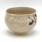 Side view of the hand-painted Kyo-yaki chawan showing a dark branch with green leaves and subtle white accents against the warm beige glaze