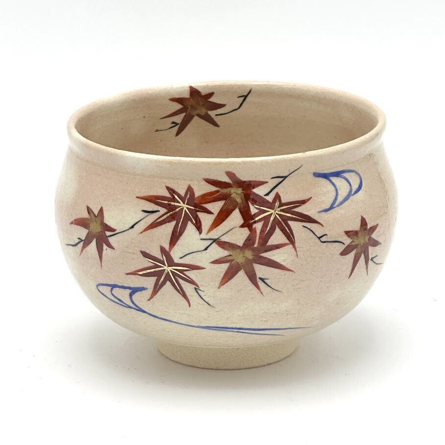 Hand-painted Kyo-yaki matcha bowl featuring the Momiji Ryusui motif with red and brown autumn maple leaves drifting along blue flowing water on a warm beige glaze