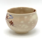 Angled view of the Kyo-yaki Momiji Ryusui chawan showing its rounded profile, warm beige glaze, and partial hand-painted maple leaf and flowing water motif