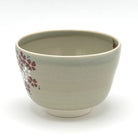 Angled view of the Kyo-yaki Sakurazume chawan showing its rounded profile, soft beige glaze, and partial hand-painted cherry blossom decoration