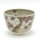 Hand-painted Kyo-yaki matcha bowl featuring the Sakurazume motif with dense pink and white cherry blossoms surrounding a textured tree trunk on a soft beige glaze
