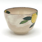 Side view of the hand-painted Kyo-yaki matcha bowl showing yellow yuzu fruit and dark green leaves against the softly textured ivory glaze