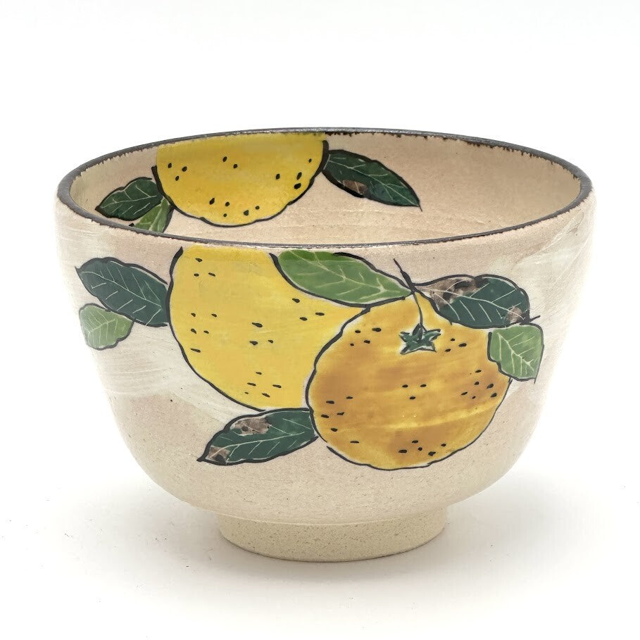 Hand-painted Kyo-yaki matcha bowl featuring bright yellow yuzu fruit with green leaves on a warm ivory glaze