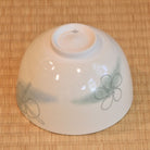 Angled underside view of the Musubi Wakakusa matcha bowl showing green and brown knot motifs around the white exterior and raised foot.