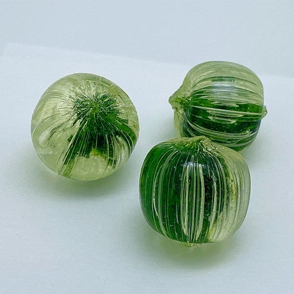 Three green and clear striped glass beads on a white background