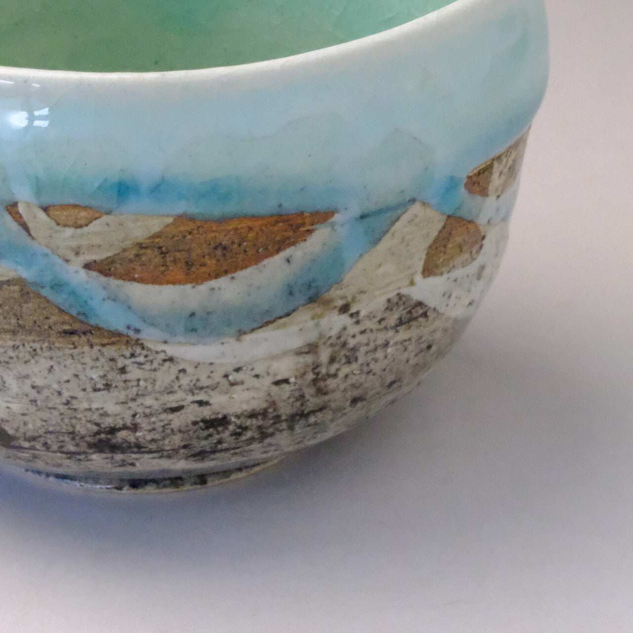 Close-up detail of the katakuchi bowl showing the flowing sky-blue band, warm brown accents, and speckled textured lower glaze.