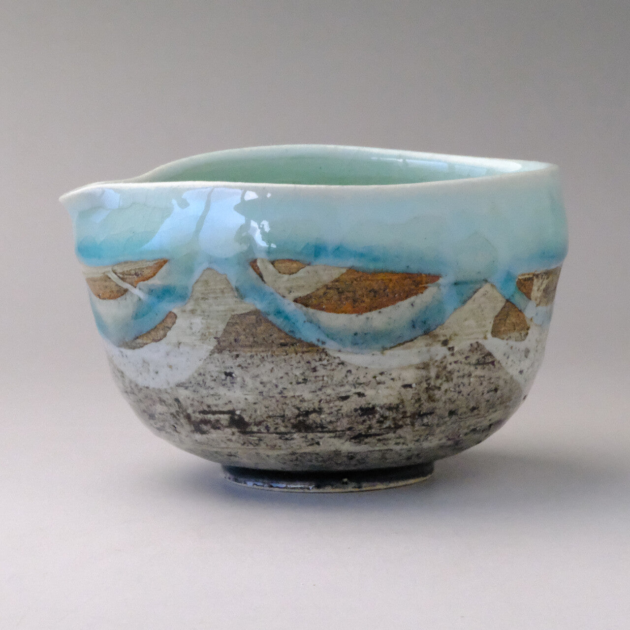 Side profile of the mint blue pouring bowl showing the rounded form and layered blue and earth-tone exterior glaze.