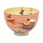 Front view of a hand-painted Mitani Fukuho Kyo Ware matcha bowl with Santa in a gift-filled sleigh, a reindeer, falling snow, and stockings on a warm pink glaze.