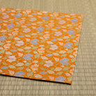 Folded edge of the orange silk dashibukusa showing its hand-sewn construction and repeating chrysanthemum pattern.