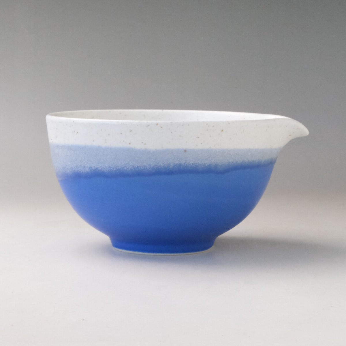 Right side profile of the Ocean Blue Mino Ware katakuchi bowl highlighting its curved pouring spout and two-tone blue and white glaze