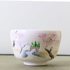 Front view of a hand-painted Kyo Ware matcha bowl decorated with cherry blossoms, a winding stream, a red bridge, and fresh green trees.