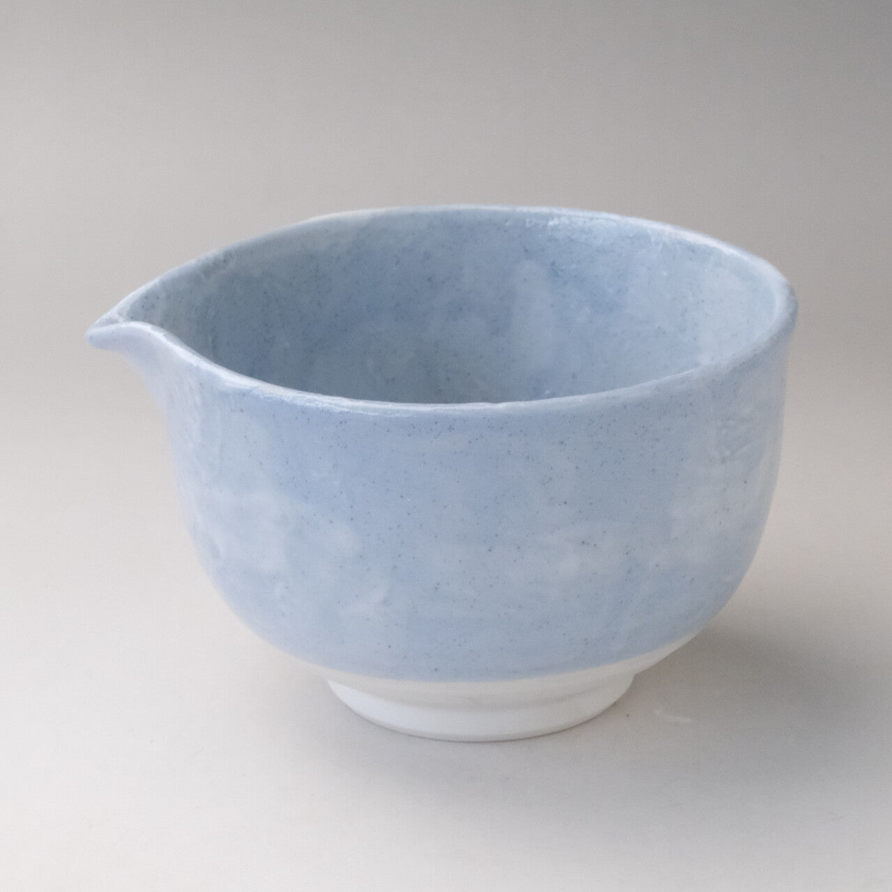 Three-quarter view of a pale blue Mino Ware katakuchi matcha bowl with a pouring spout and softly clouded glaze.