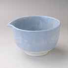 Three-quarter view of a pale blue Mino Ware katakuchi matcha bowl with a pouring spout and softly clouded glaze.