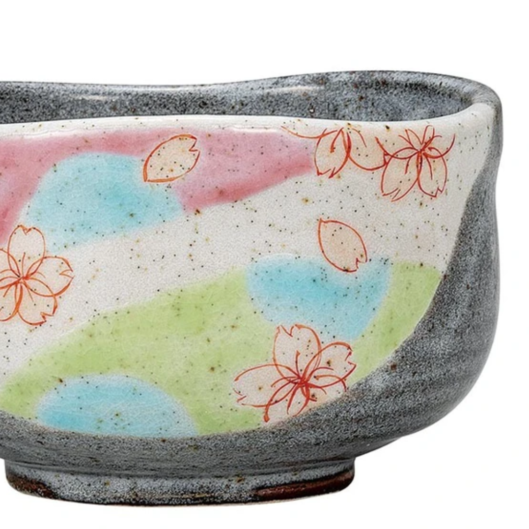 Left angled view of the Kutani Ware matcha bowl showing its softly irregular rim, dark gray outer body, and pastel sakura design.