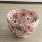 Angled side view of the Kyo Ware chawan showing pink peach blossoms, gold details, and the finely patterned surface continuing around the exterior.