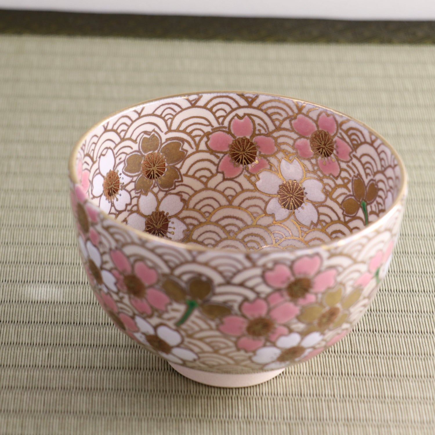 Angled side view of the Kyo Ware chawan showing pink peach blossoms, gold details, and the finely patterned surface continuing around the exterior.