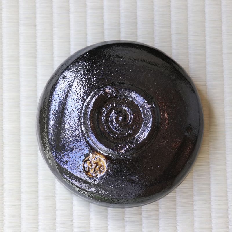 A round glossy black ceramic bowl with a spiral design on the bottom, placed on a light beige textured mat.