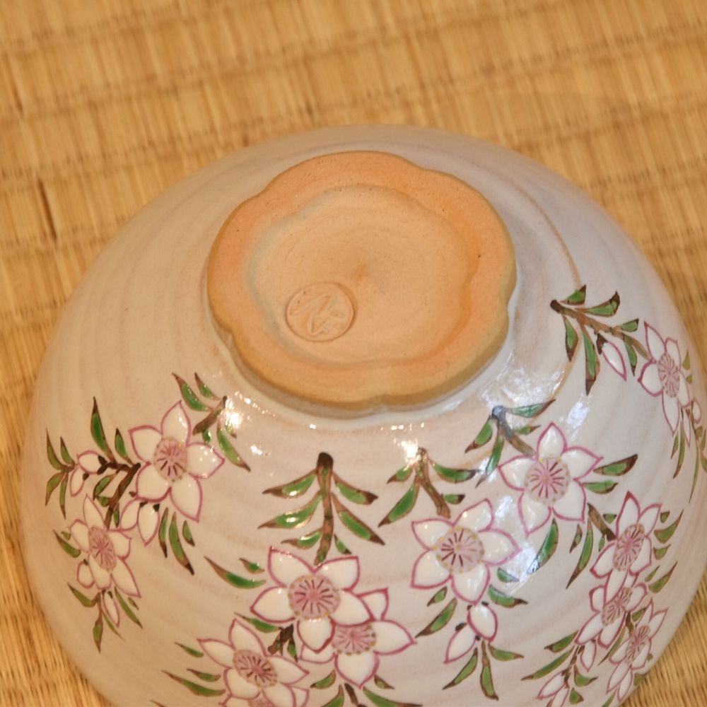 Angled underside view of the Ryoji Nakamura matcha bowl showing peach blossom branches surrounding its flower-shaped foot.
