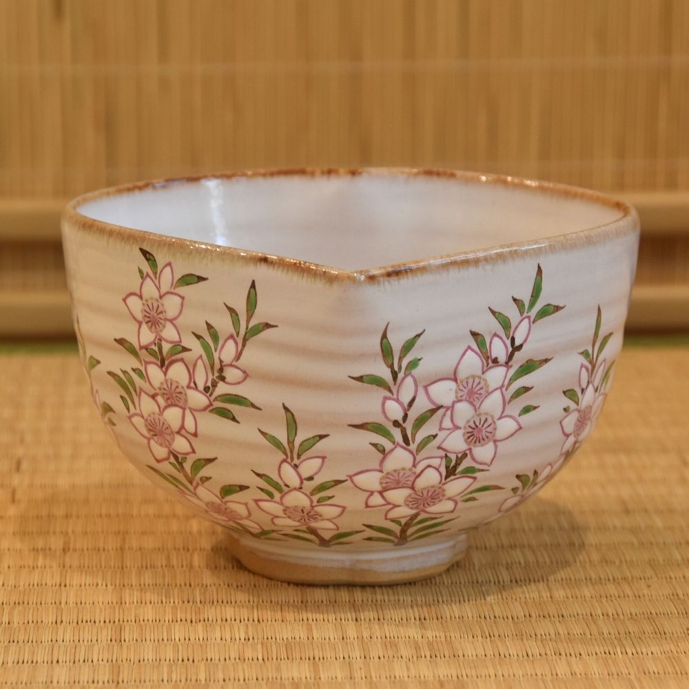 Front view of a hand-painted Kyo Ware katakuchi matcha bowl by Ryoji Nakamura with pale pink peach blossoms and a petal-shaped rim.