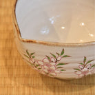 Close-up of the pouring lip, warm brown rim, and hand-painted peach blossoms on the Ryoji Nakamura katakuchi matcha bowl.