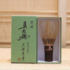 Ryosai Kubo handcrafted Takayama chasen made from Japanese black bamboo with Coral #3 thread, displayed beside its presentation box