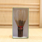 Ryosai Kubo black bamboo Takayama chasen with Dark Red #4 thread displayed upright inside its green presentation box