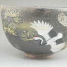 Side view highlighting a white crane in flight against the mottled charcoal glaze with plum blossoms and fine gold-toned accents.