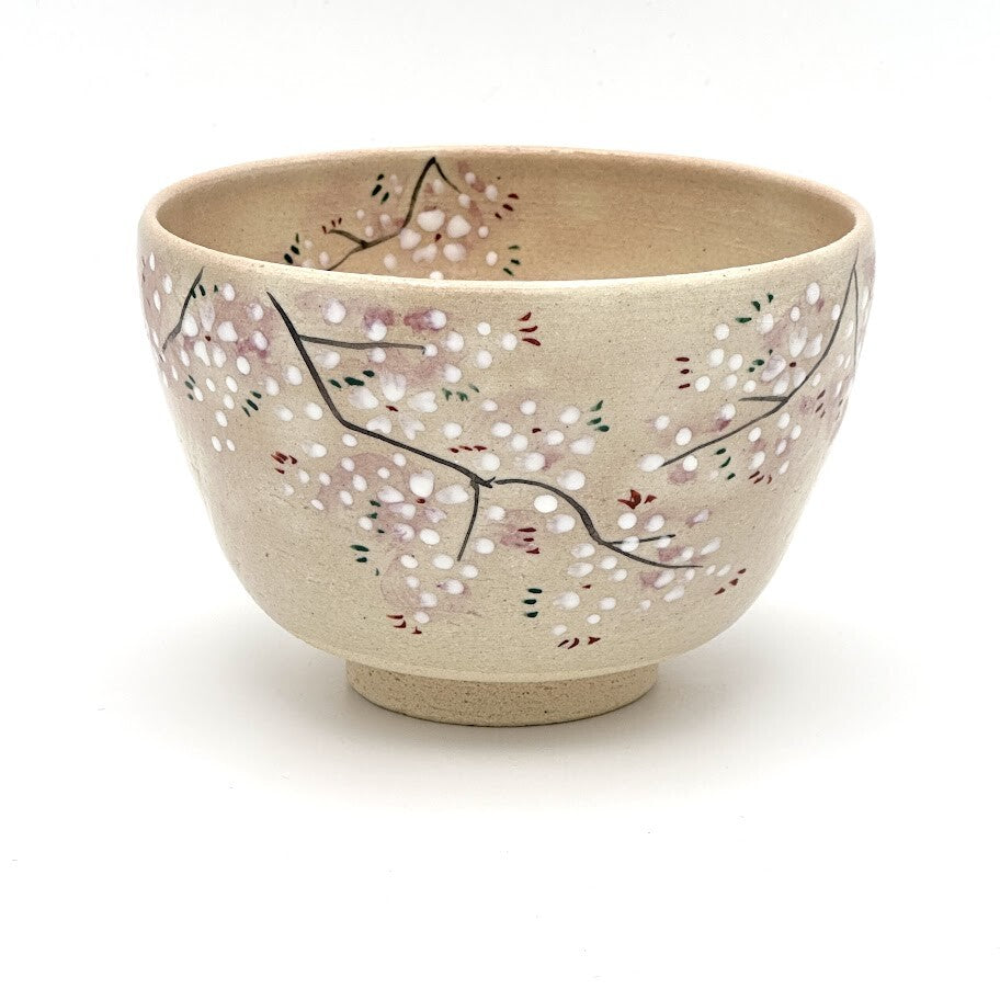Hand-painted Kyo Ware matcha bowl featuring delicate pink and white cherry blossoms on branching stems over a warm beige glaze