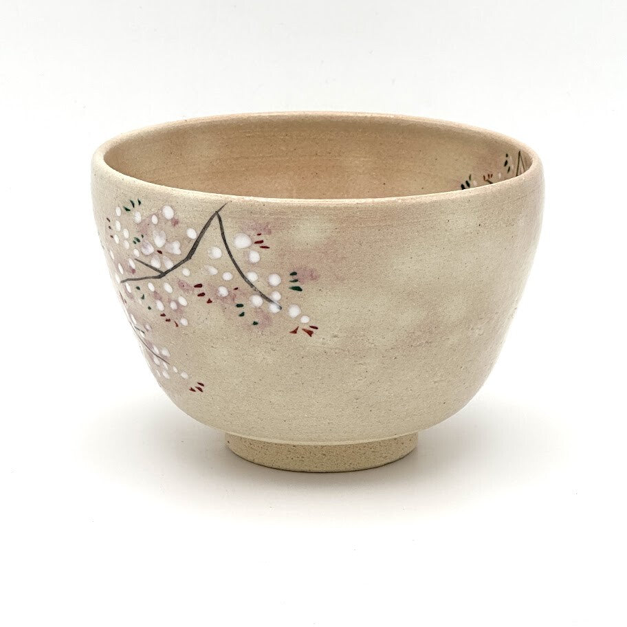 Angled view of the hand-painted Sakura Kyo Ware chawan showing delicate cherry blossom branches and warm beige ceramic surface