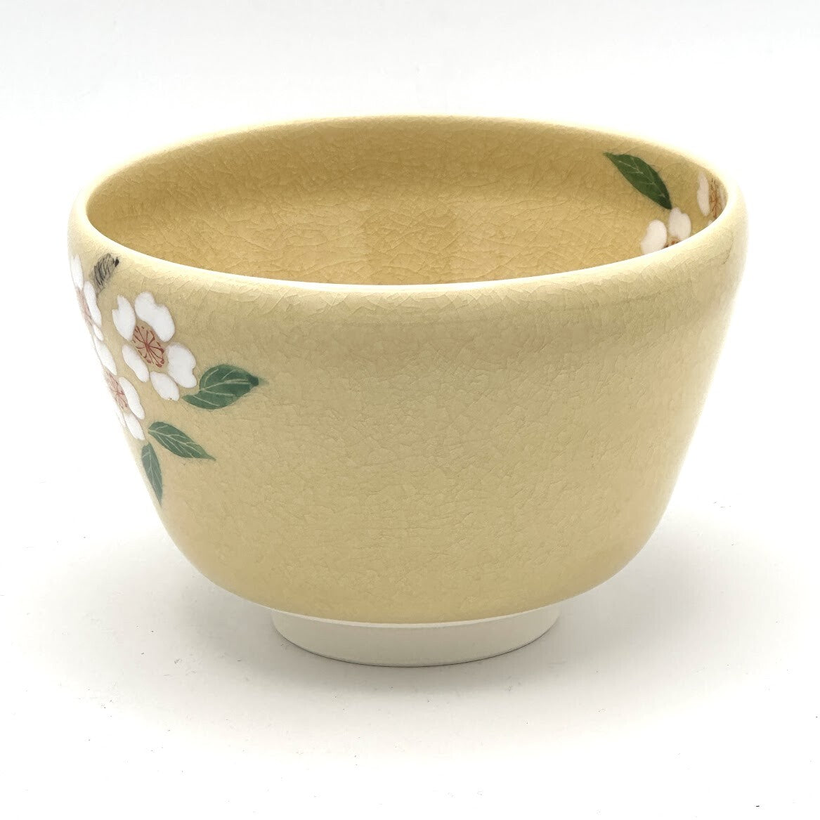 Left-side view of the hand-painted matcha bowl with cherry blossoms wrapping around the bowl and a leaf detail near the rim.