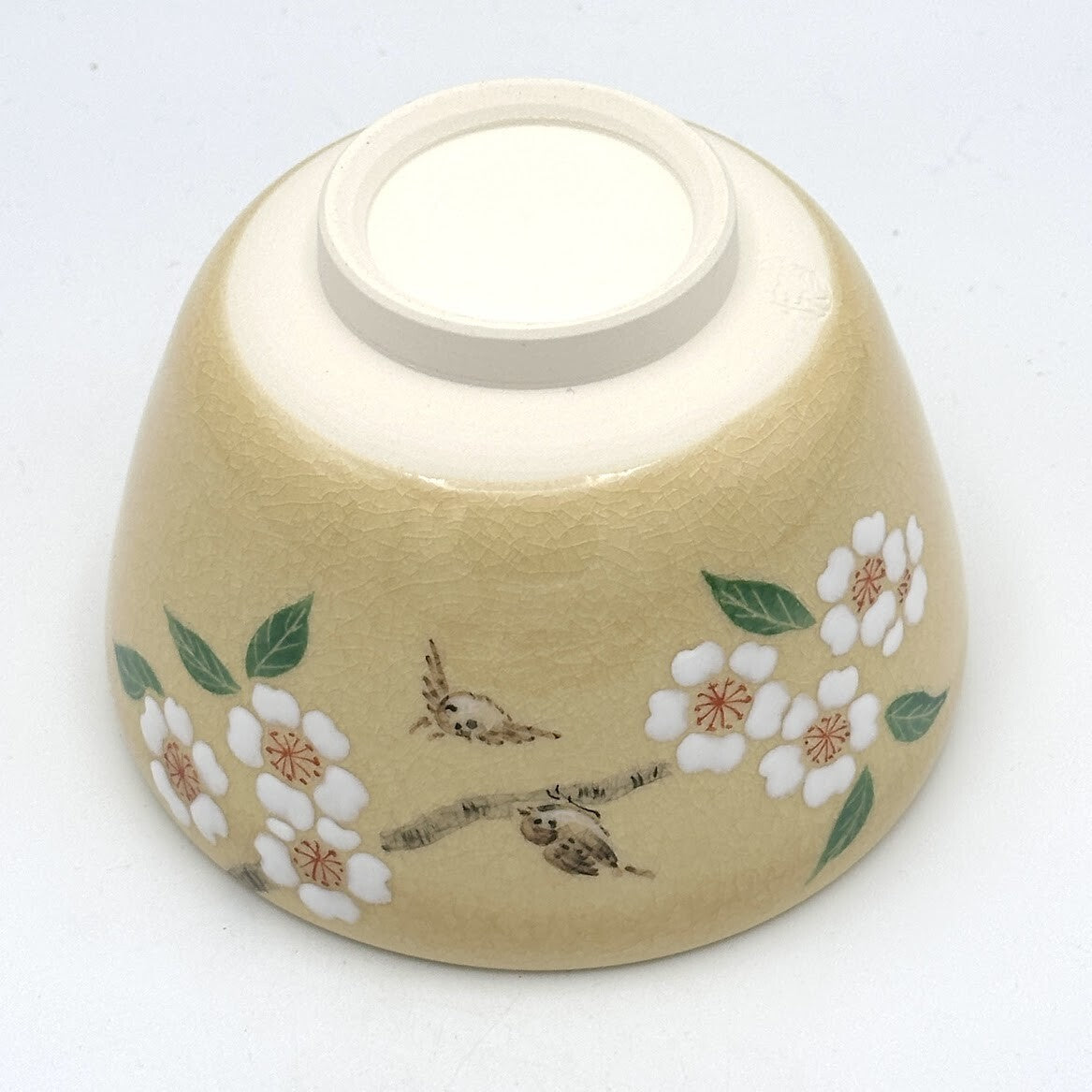 Underside of the handcrafted matcha bowl showing the foot ring and hand-painted cherry blossoms and songbirds on the exterior.
