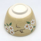 Underside of the handcrafted matcha bowl showing the foot ring and hand-painted cherry blossoms and songbirds on the exterior.