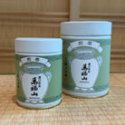 Two green tea tins with white labels on a wooden surface