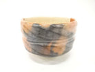 Side view of the Shoraku Sasaki Kotobuki Red Raku chawan showing its warm red-orange surface, hand-formed shape, and flowing dark charcoal glaze