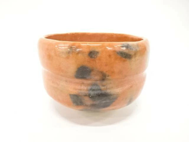 Front view of the Matsukaze Red Raku matcha bowl with persimmon-red glaze, smoky charcoal markings, horizontal ridges, and a pale foot.