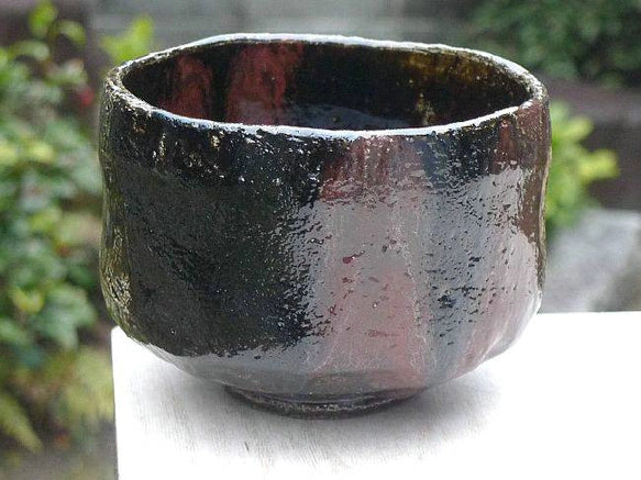 Angled front view of the Kakuyo Black Raku matcha bowl showing its irregular rim, rounded form, and reddish-brown glaze variation.