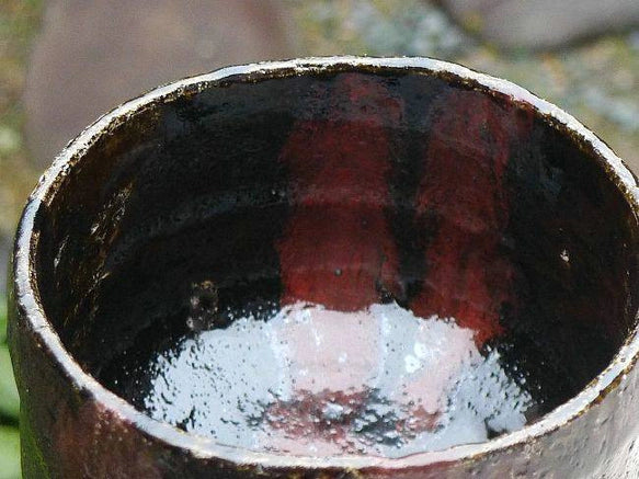 Top view of the Kakuyo matcha bowl showing its deep black interior with copper-red and dark plum-toned firing effects.