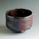 Front view of the Shuraku Kiln Kakuyo Black Raku matcha bowl with a lustrous black glaze and copper-red and bronze-toned firing effects.
