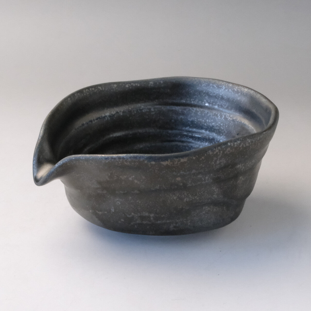 Three-quarter view of a smoky silver-gray Mino Ware katakuchi matcha bowl with a pointed pouring spout and textured ridged surface.