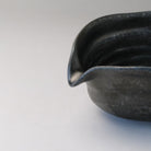 Close-up of the pointed pouring spout and dark ridged interior of the silver-gray katakuchi matcha bowl.
