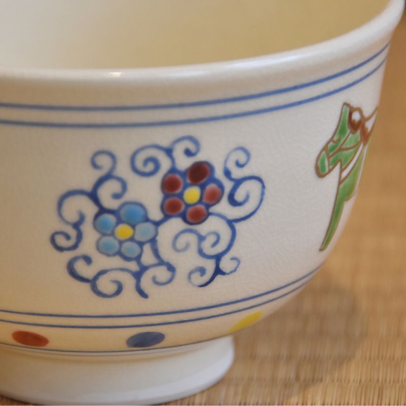 Close-up of blue and red arabesque scrollwork beside a green horse on the hand-painted matcha bowl.