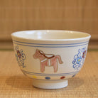Side view of the Kyo Ware matcha bowl showing a brown zodiac horse between colorful plum blossom and arabesque decorations.