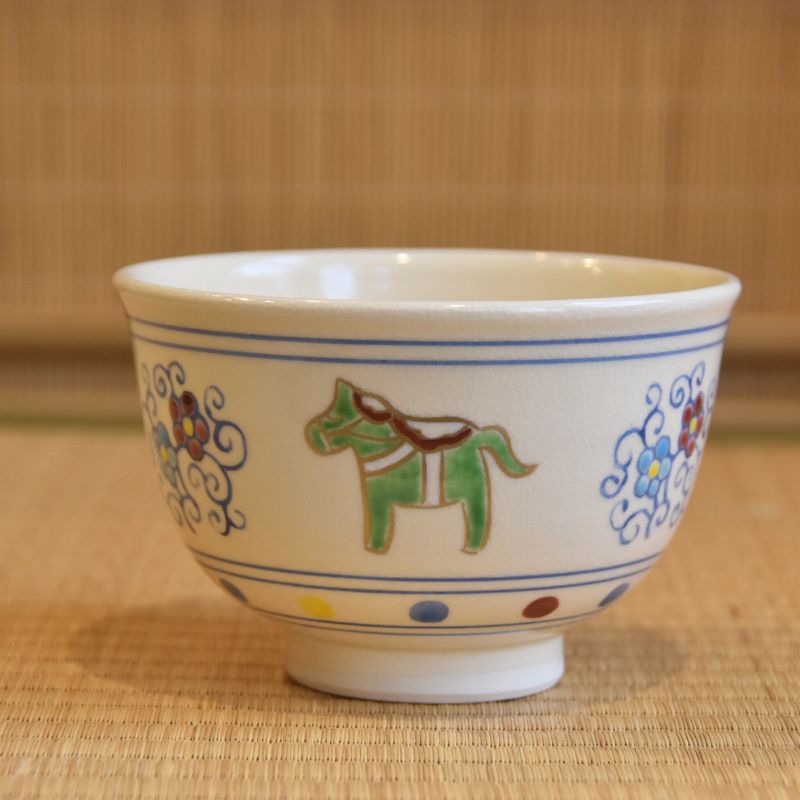 Front view of a hand-painted Kyo Ware matcha bowl with a green zodiac horse, colorful plum blossoms, and blue arabesque motifs.
