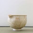 Side view of the Tōan Hana-Kesshō golden flower katakuchi bowl showing its rounded form, pouring spout, and layered cream crystalline glaze