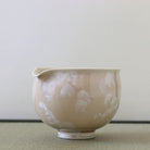 Side view of the Tōan Hana-Kesshō natural beige katakuchi bowl showing its rounded form, pouring spout, and delicate ivory flower crystal glaze patterns